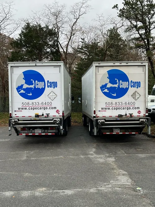 Two Cape Cargo box trucks backed up to load, showing the company phone number and logo
